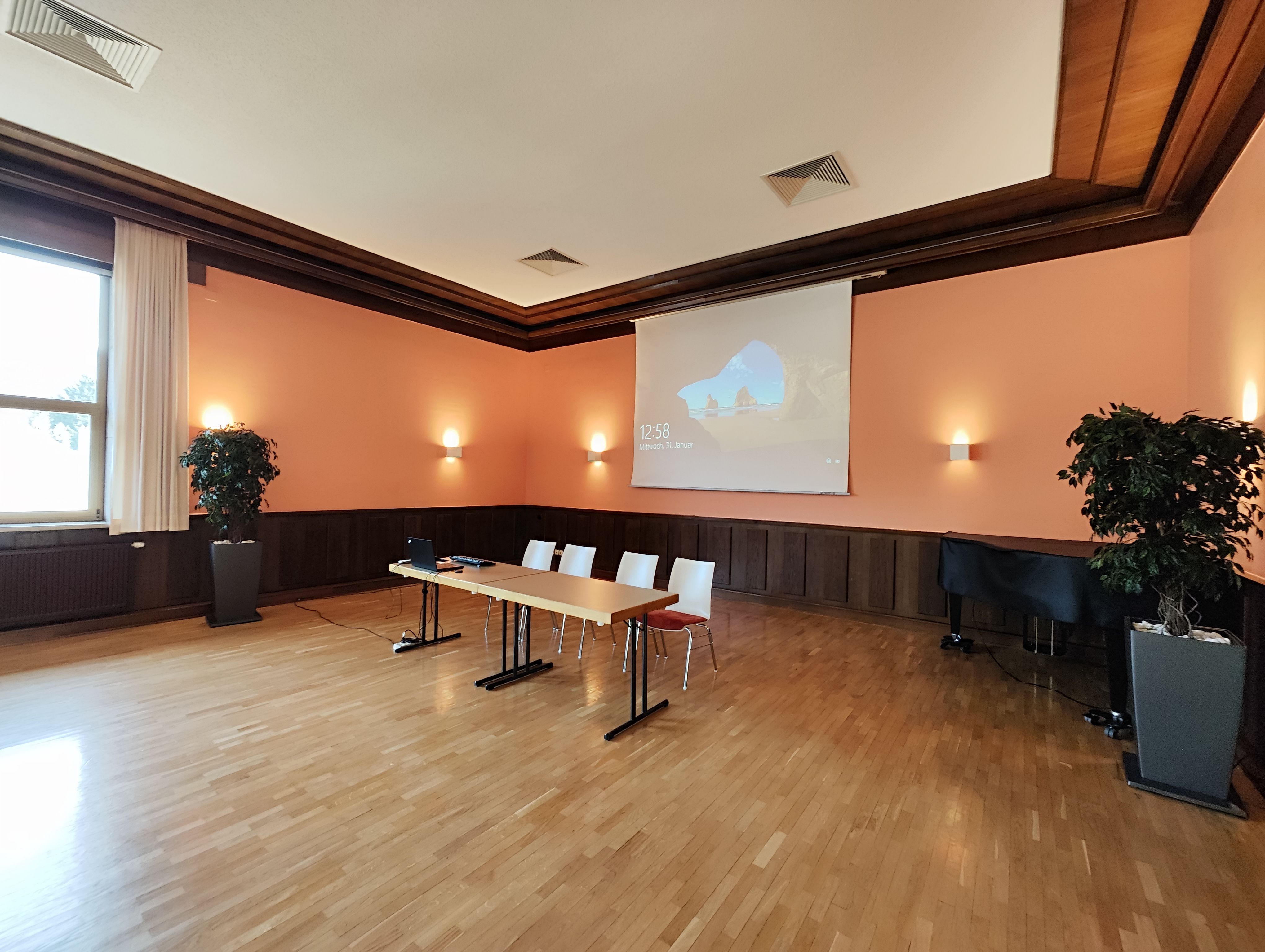 Kleiner Saal -  Ein heller Raum in orange gehalten mit Tisch und Stühlen. im Hintergrund die Leinwand für den Beamer.