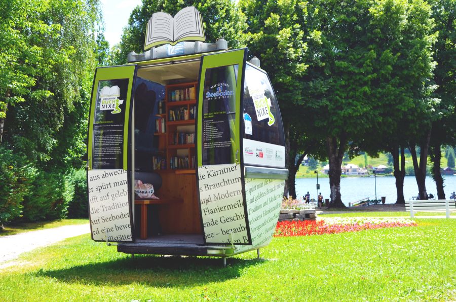 Die Buchnixe ist eine Gondel bei der die Türen geöffnet werden können, Sie ist in der Farbe Grün. Im innenbereich gibt es einen Sitzmöglichkeit und ein angebrachtes Regal mit Büchern die getauscht oder kostenfrei mitgenommen werden können. 