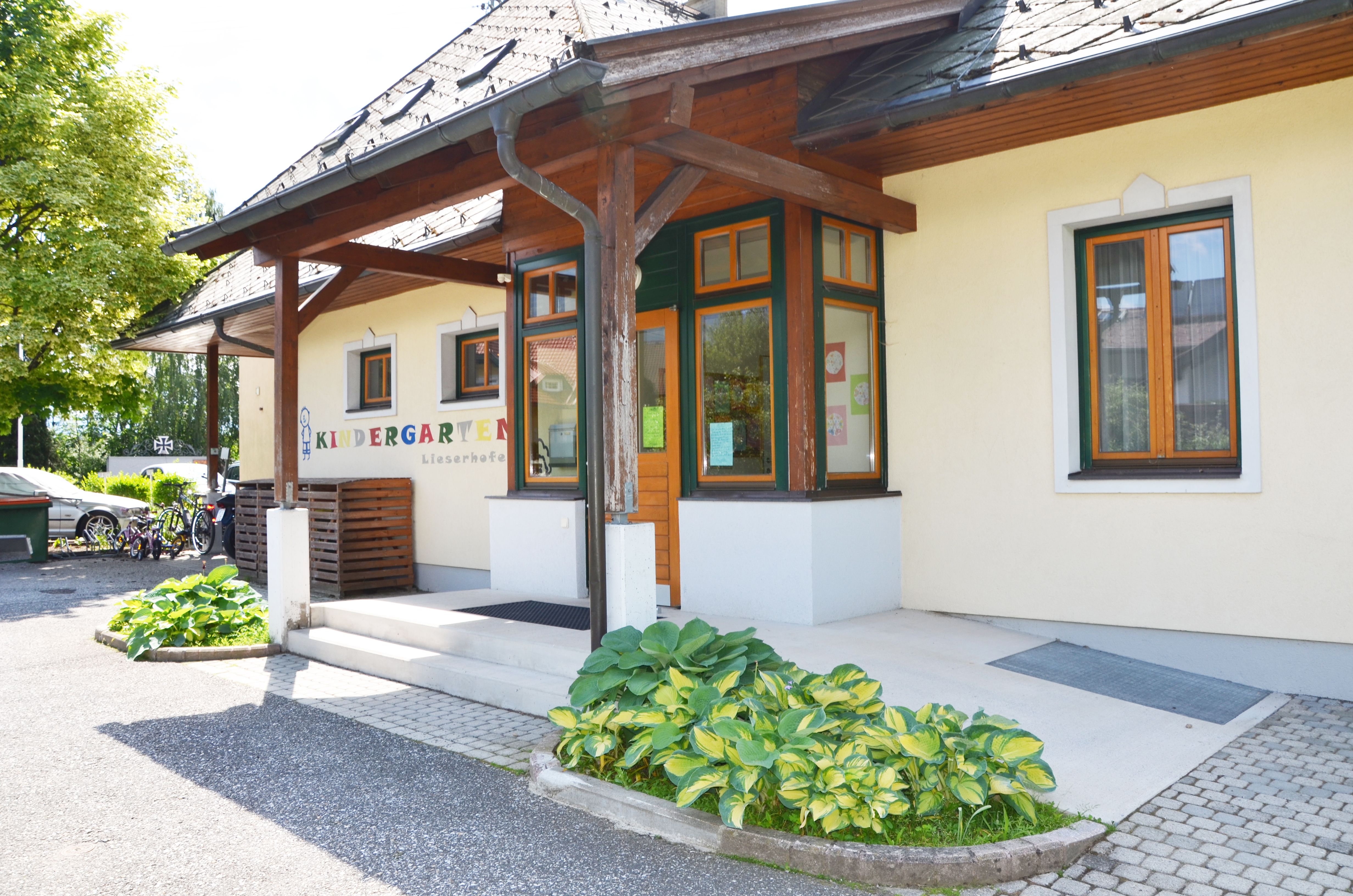 Das Gebäude vom Kindergarten Lieserhofen hat eine gelbe Fassade mit einem einladenden Eingangsbereich. Das Logo mit bunten Buchstaben wurde auf die Fassade gemalt.