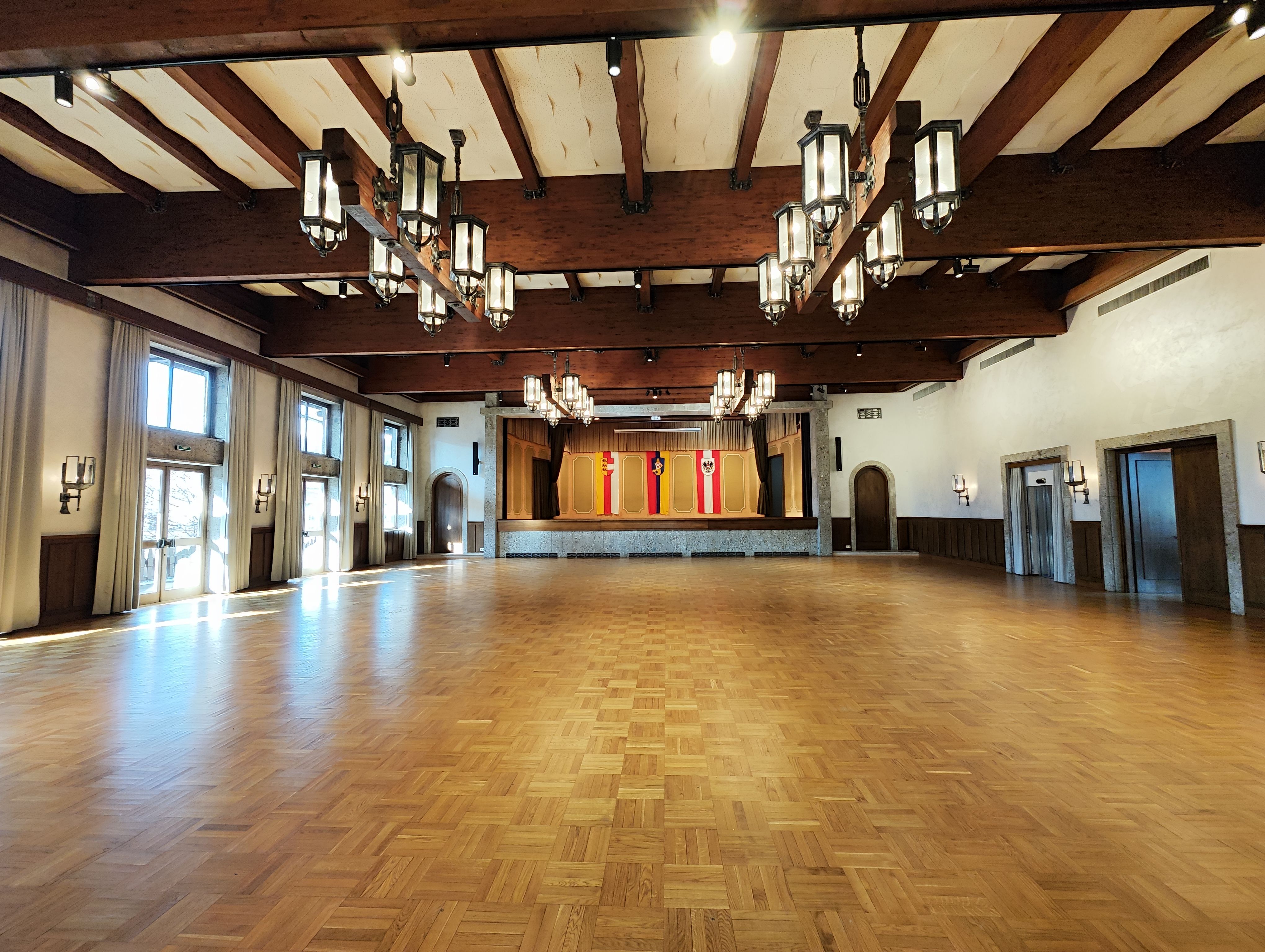 Der Große Saal - Fläche mit Holzboden und Bühne im Hintergrund 3 Fahnen von Österreich, Kärnten und Seeboden