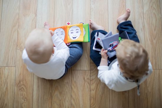 Zwei Babys sitzen am Boden und spielen mit Babybüchern