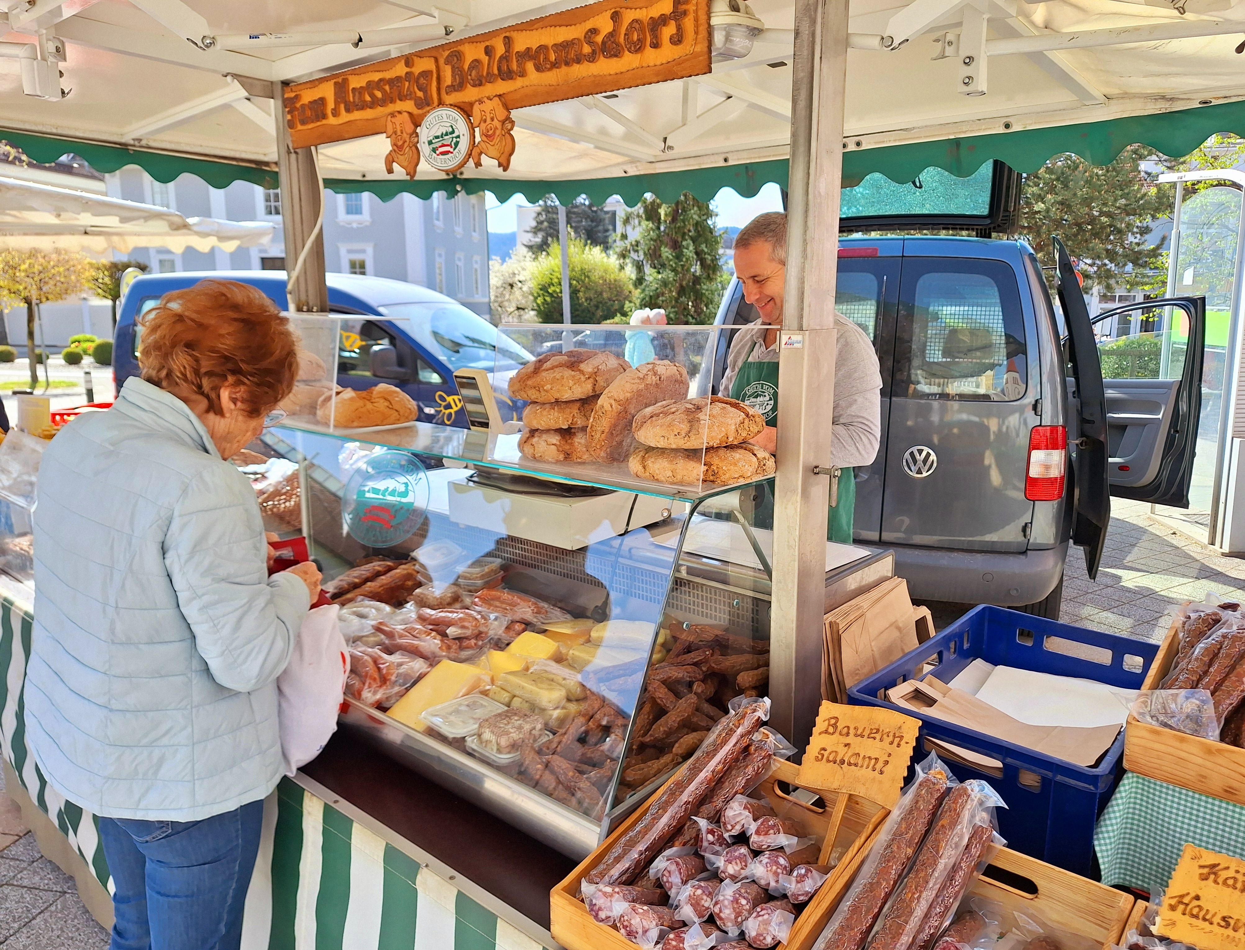 Ein Marktstand vom Bauern, es gibt Speck, Würste und Salami sowie Brot und verschiedene Fleischerzeugnisse.