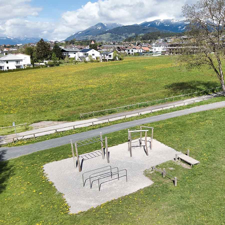 Die Calisthenicsanlage am Klauberpark eigente sich zum Trainieren mit dem eigenen Körpergewicht. In idyllischer umgebung zwischen Wiesen und Bergen sehen Sie die Anlage aus Holz mit den verschiedenen Geräten zum trainieren auf Schotter untergrund. 