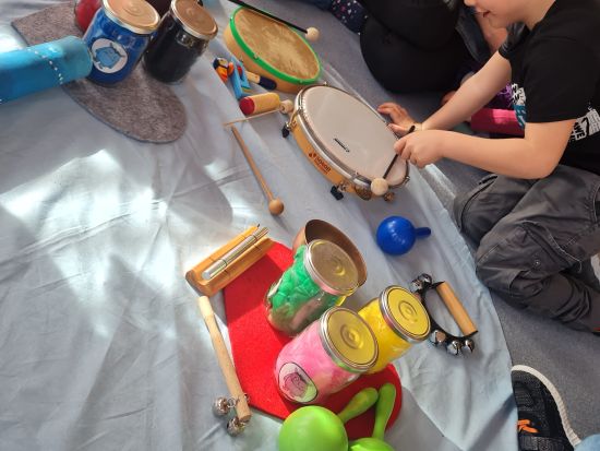 Motopädagogik und Musik – die Kinder lernen selbstständig Lösungen zu finden. Auf dem Bild sitzt ein Kind neben Musikinstrumenten und bunten Gläsern uns erstellt eine eigenes Farb- und Musikkonzept.