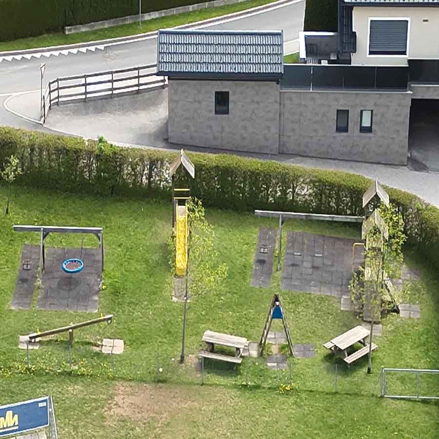 Der Spielplatz der VS Treffling aus der Luft. Er verfügt über einen gelebe Rutsche und zwei Schaukeln sowie einer Netzschaukel. 